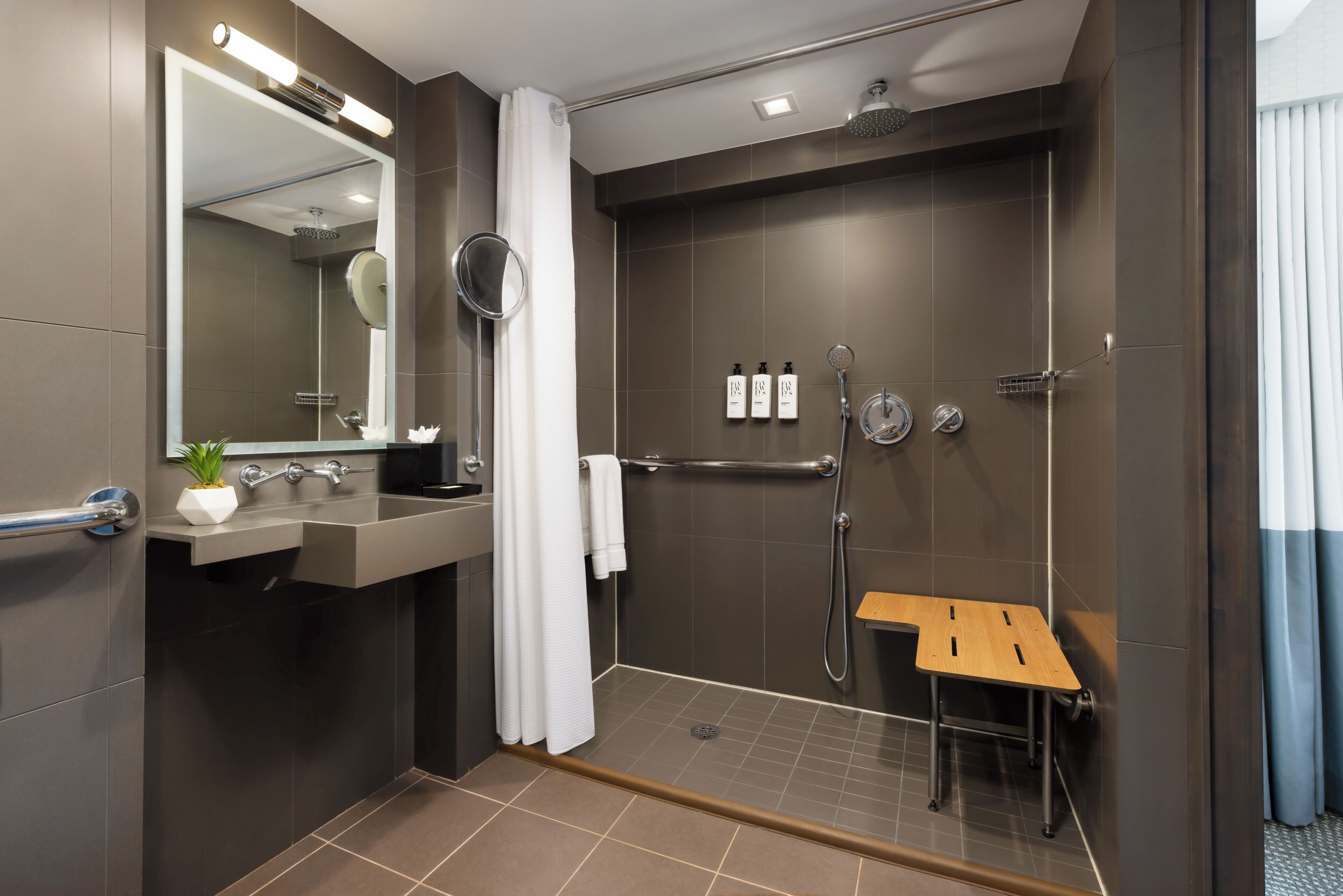 Une salle de bain moderne équipée d’une douche, d’un lavabo, d’un miroir et d’un petit tabouret en bois.