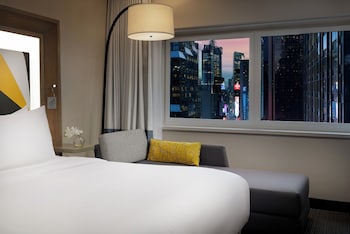 A person using an exercise bike in a room with a window, a clock, and a view of buildings outside. at M Social Hotel New York Times Square