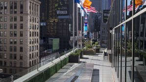 A modern urban plaza with a reflective water feature, surrounded by high-rise buildings and flags.