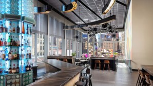 A modern bar with a curved counter, bar stools, and a large window offering a city view.