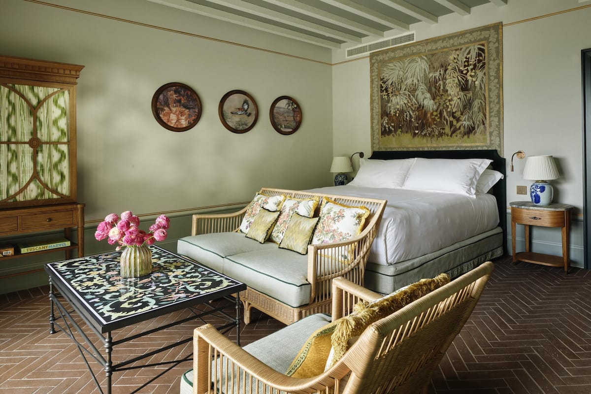 A bedroom with a bed, a sofa, a table with a vase, and a large painting on the wall.