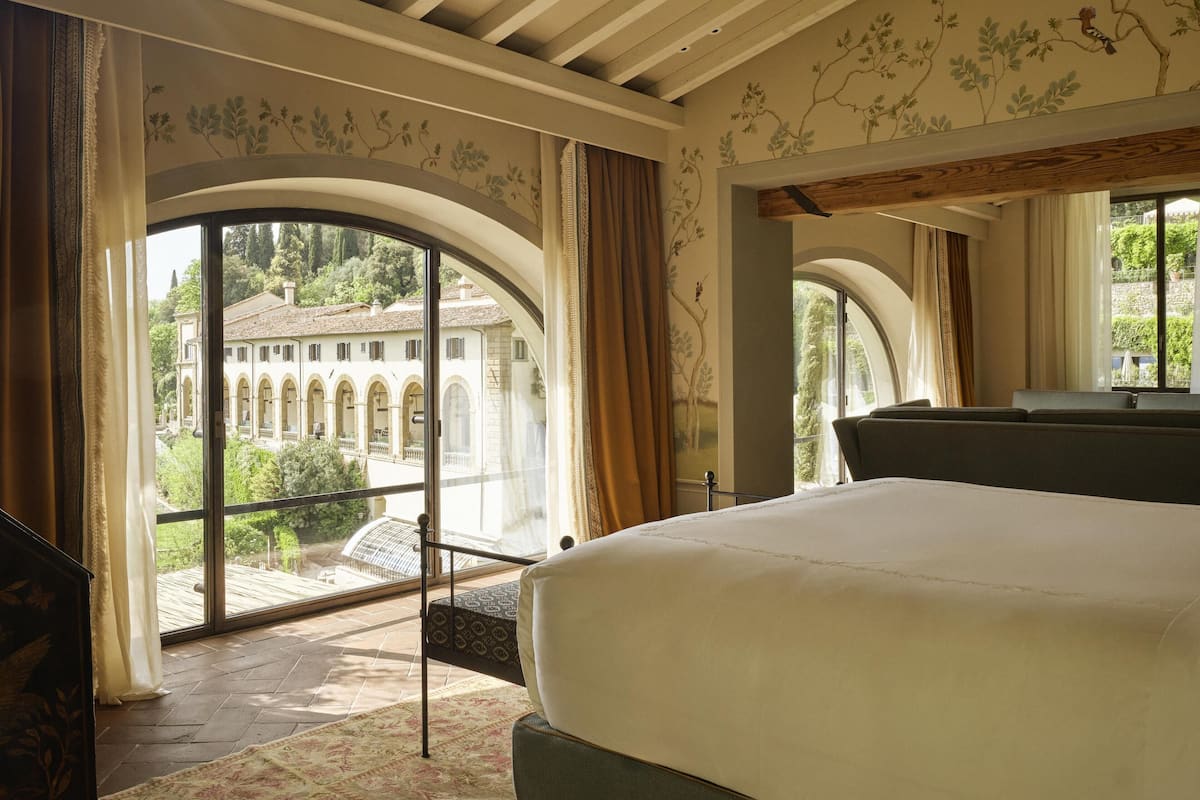 A bedroom with a large bed, arched windows, and a view of a building outside.