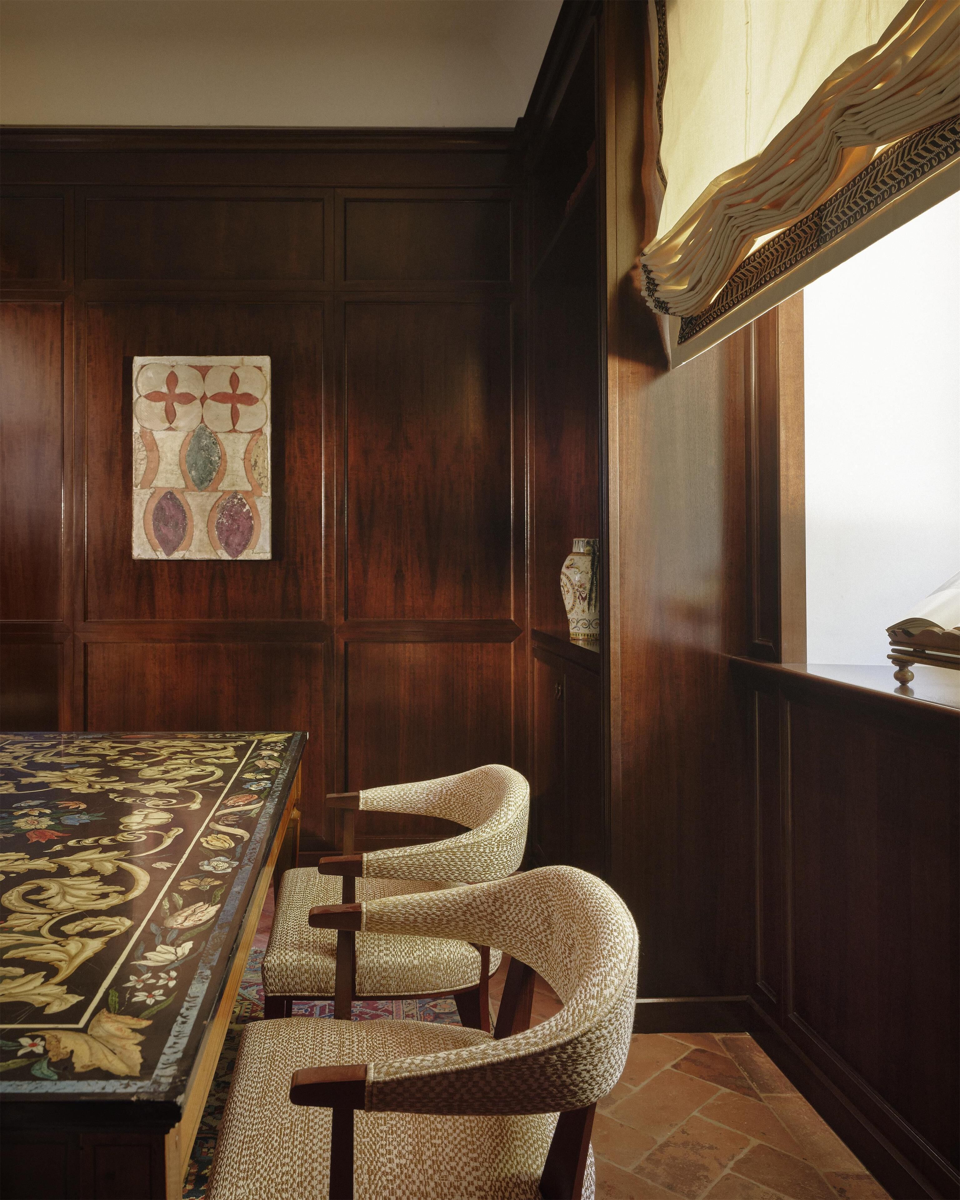 A room with a wooden paneled wall, a patterned table, and three woven chairs.