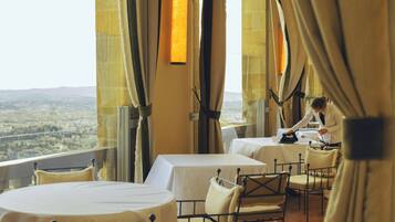 A room with a terrace overlooking a cityscape, featuring tables and chairs set up for dining.