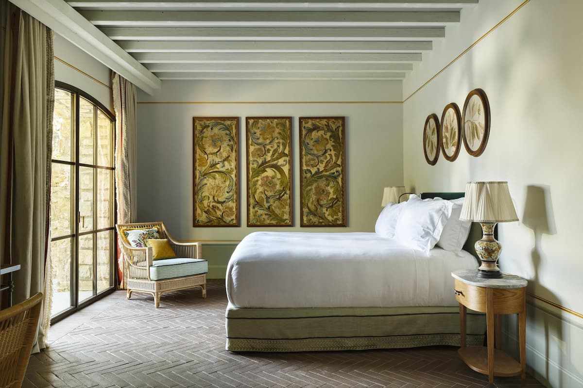 A bedroom with a large bed, a chair, a nightstand, and three framed artworks on the wall.