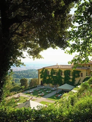 A building with a garden and outdoor seating area, surrounded by trees. - Villa San Michele, A Belmond Hotel, Florence (Fiesole)