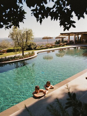 A swimming pool with clear water, surrounded by lounge chairs and umbrellas, with a view of distant hills. - Villa San Michele, A Belmond Hotel, Florence (Fiesole)