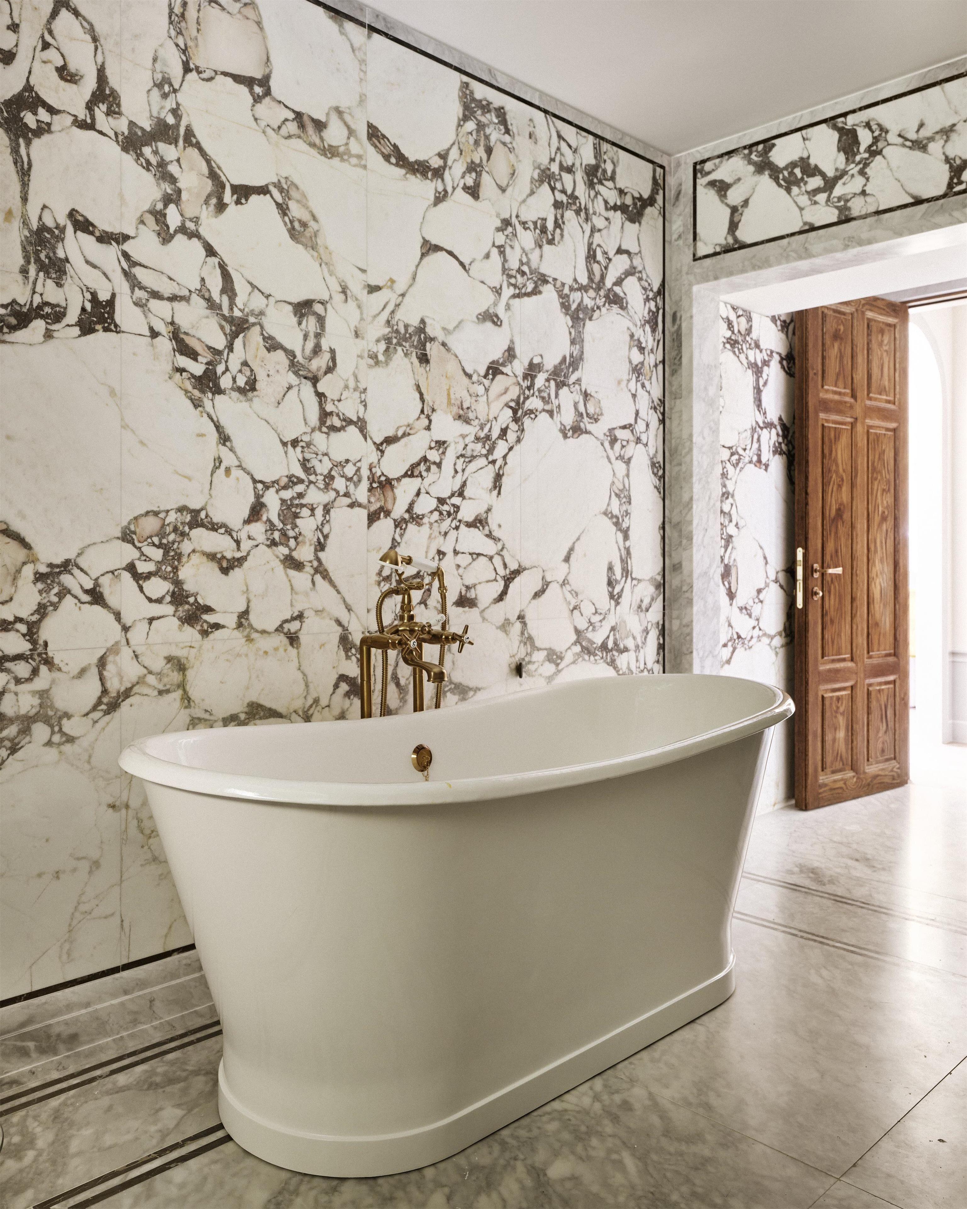 Una bañera independiente en un baño con paredes de mármol y una puerta de madera.
