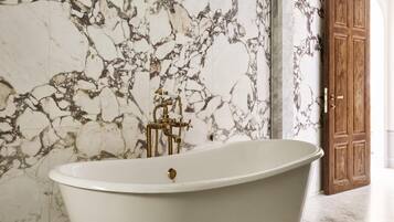 Una bañera independiente en un baño con paredes de mármol y una puerta de madera.