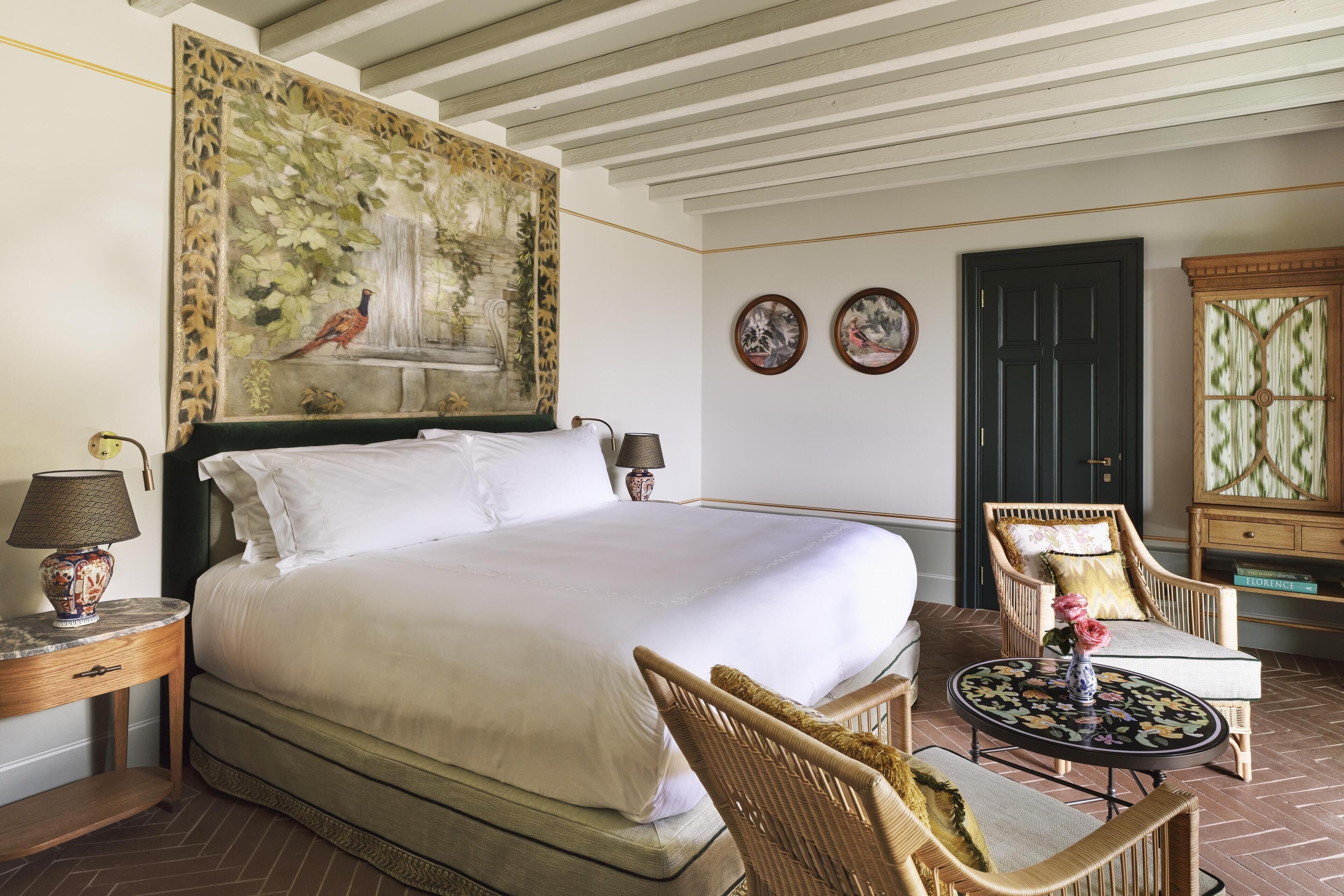 Een hotelkamer met een groot bed, een stoel, een tafeltje en een schilderij aan de muur.