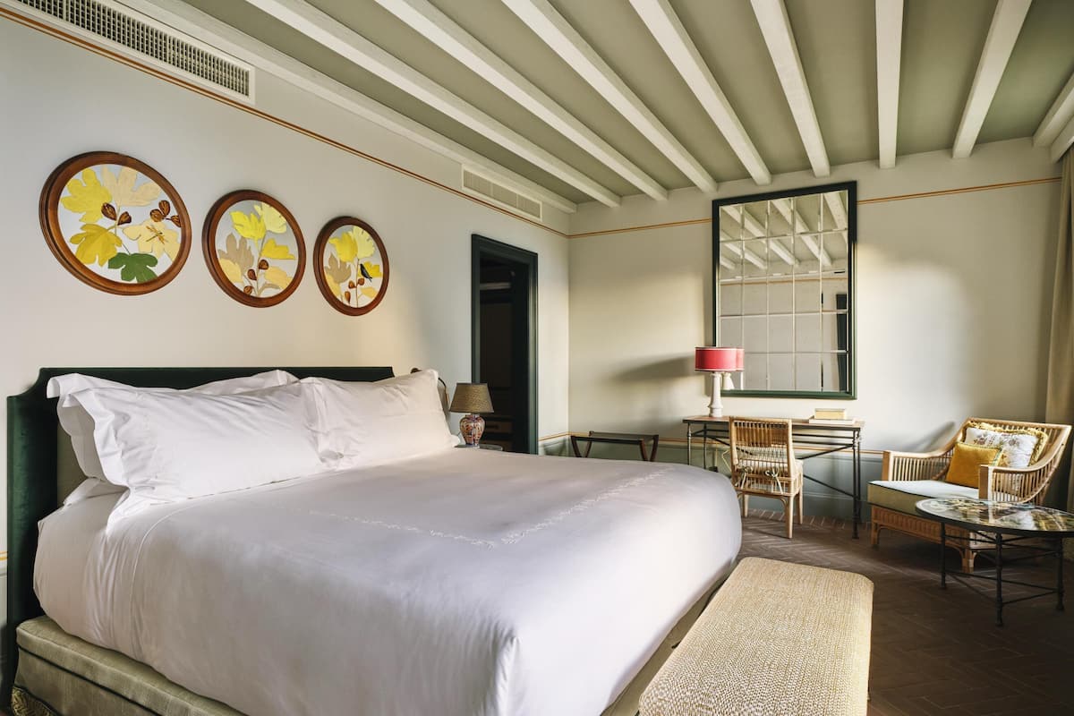 A hotel room with a large bed, a desk with a chair, a round table, and a mirror.