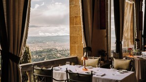 Comedor con mesas dispuestas para dos, con vistas a un paisaje urbano.