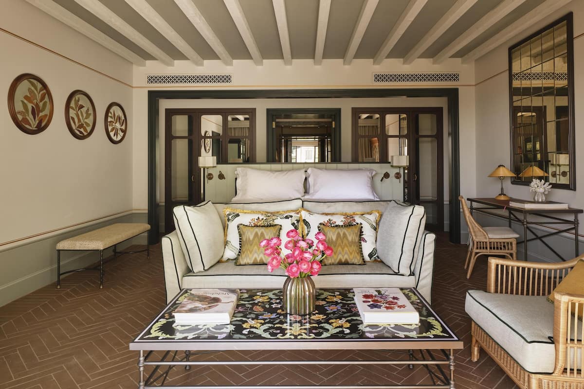 A room with a sofa, a coffee table with a vase of flowers, a bench, and a chair.
