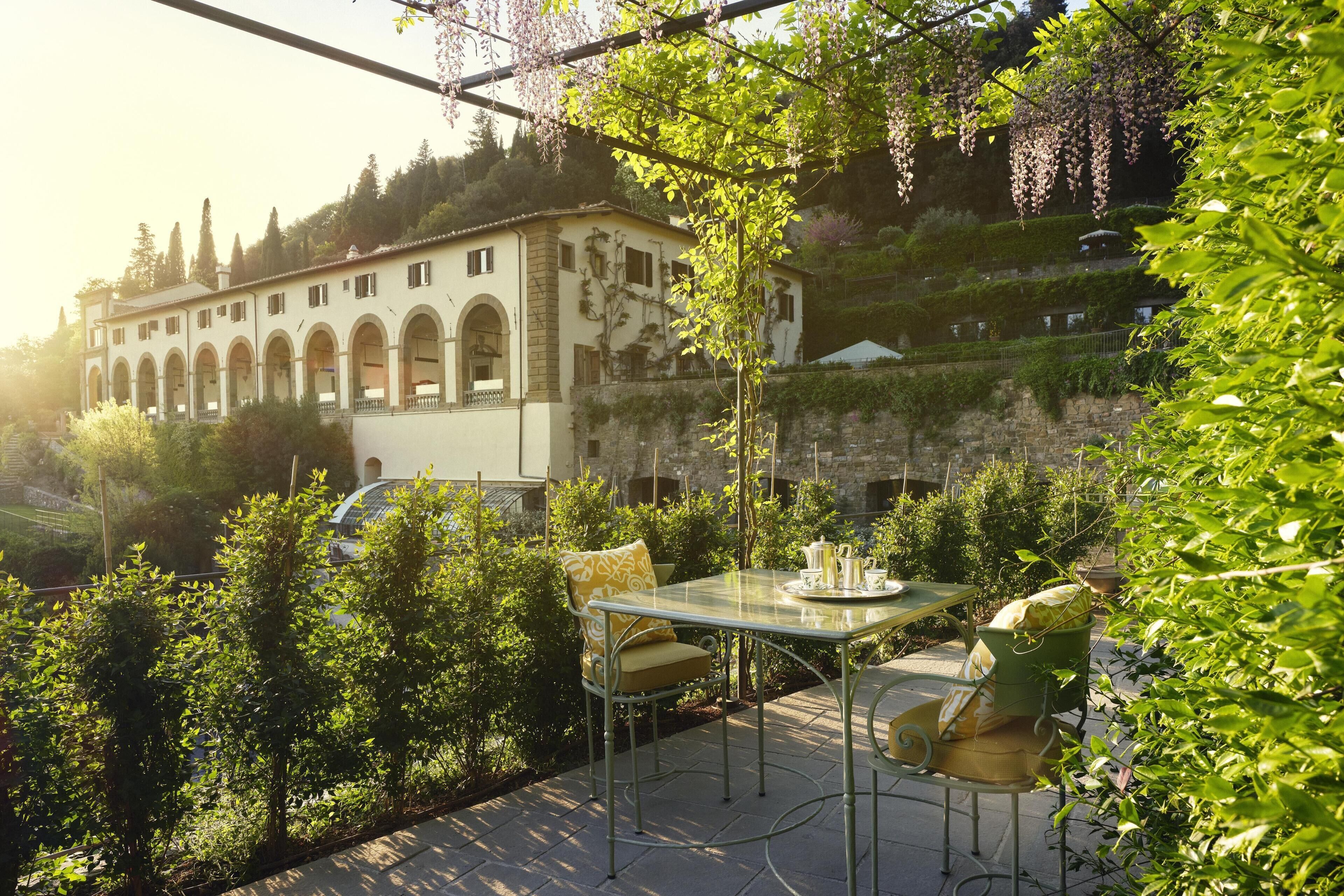 Eine Terrasse mit Tisch und Stühlen, ein Auto und ein Gebäude mit Bögen im Hintergrund.