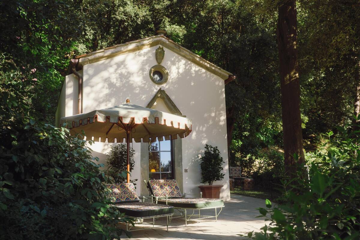 A small pavilion with a table and chairs, surrounded by greenery.
