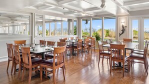 A spacious dining area with wooden tables and chairs, large windows offering views of the outdoors, and a ceiling with recessed lighting. - Carousel Resort Hotel & Condominiums (Ocean City)