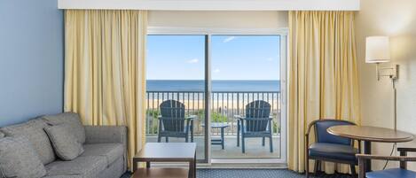 Habitación de hotel con cama, sofá, una mesita, dos sillas y un balcón con vista a la playa.