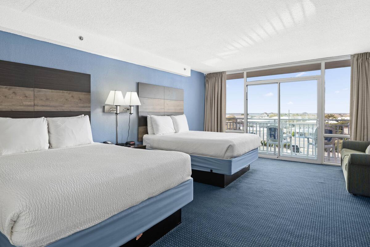 A hotel room with two beds, a large window with a view, a balcony, and a seating area.