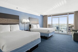 A hotel room with two beds, a large window with a view, a balcony, and a seating area.