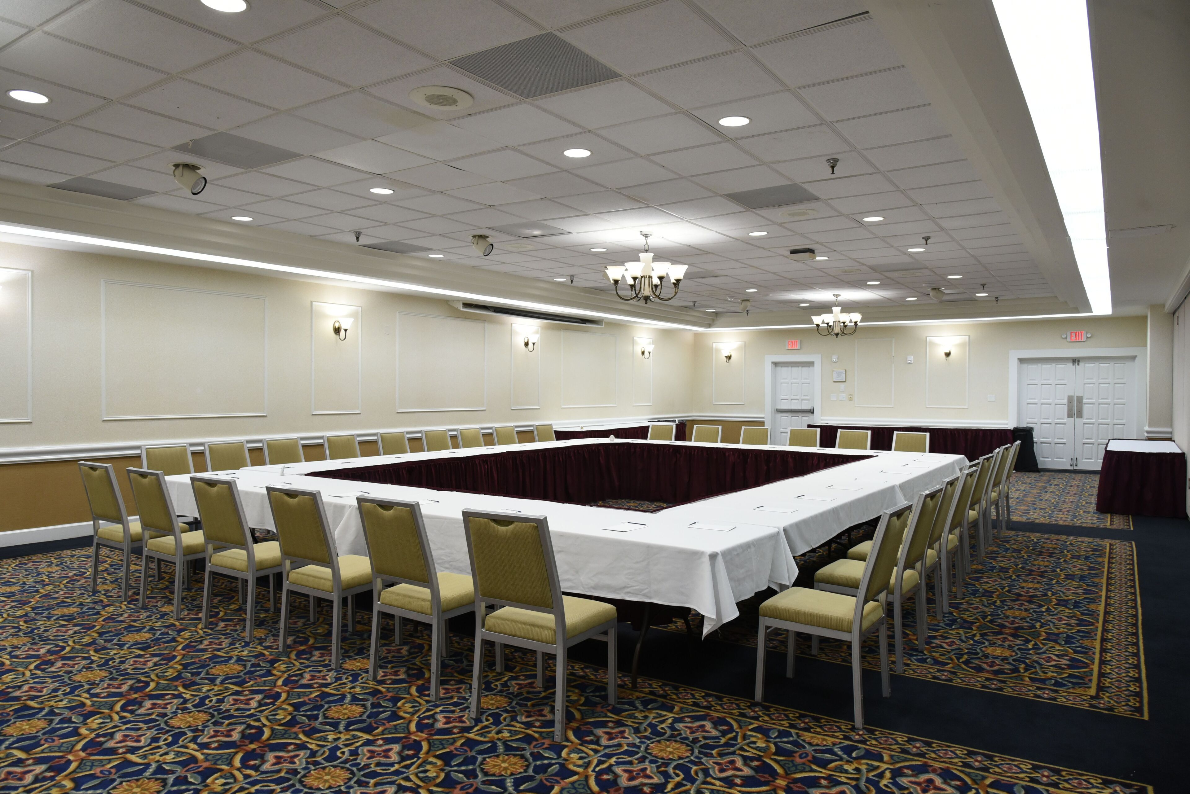 A conference room with a long table, chairs, and a patterned carpet.