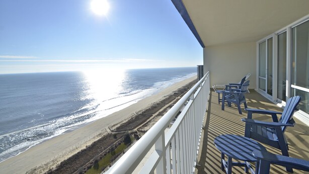A balcony with a view of the ocean, featuring a railing and several Adirondack chairs. - Carousel Resort Hotel & Condominiums (Ocean City)