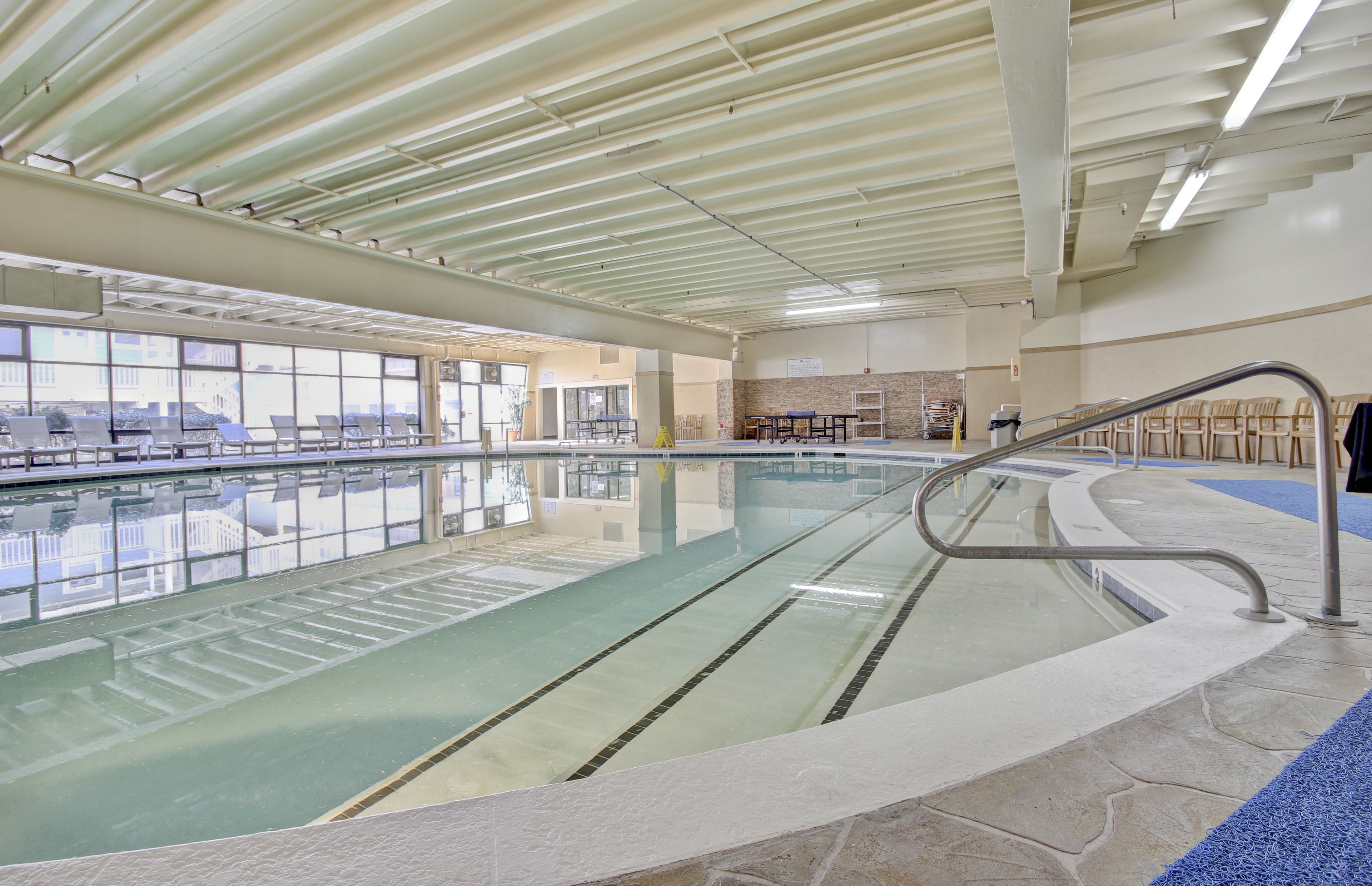 Une piscine intérieure avec des parois en verre transparent, un sol carrelé et une rambarde métallique.