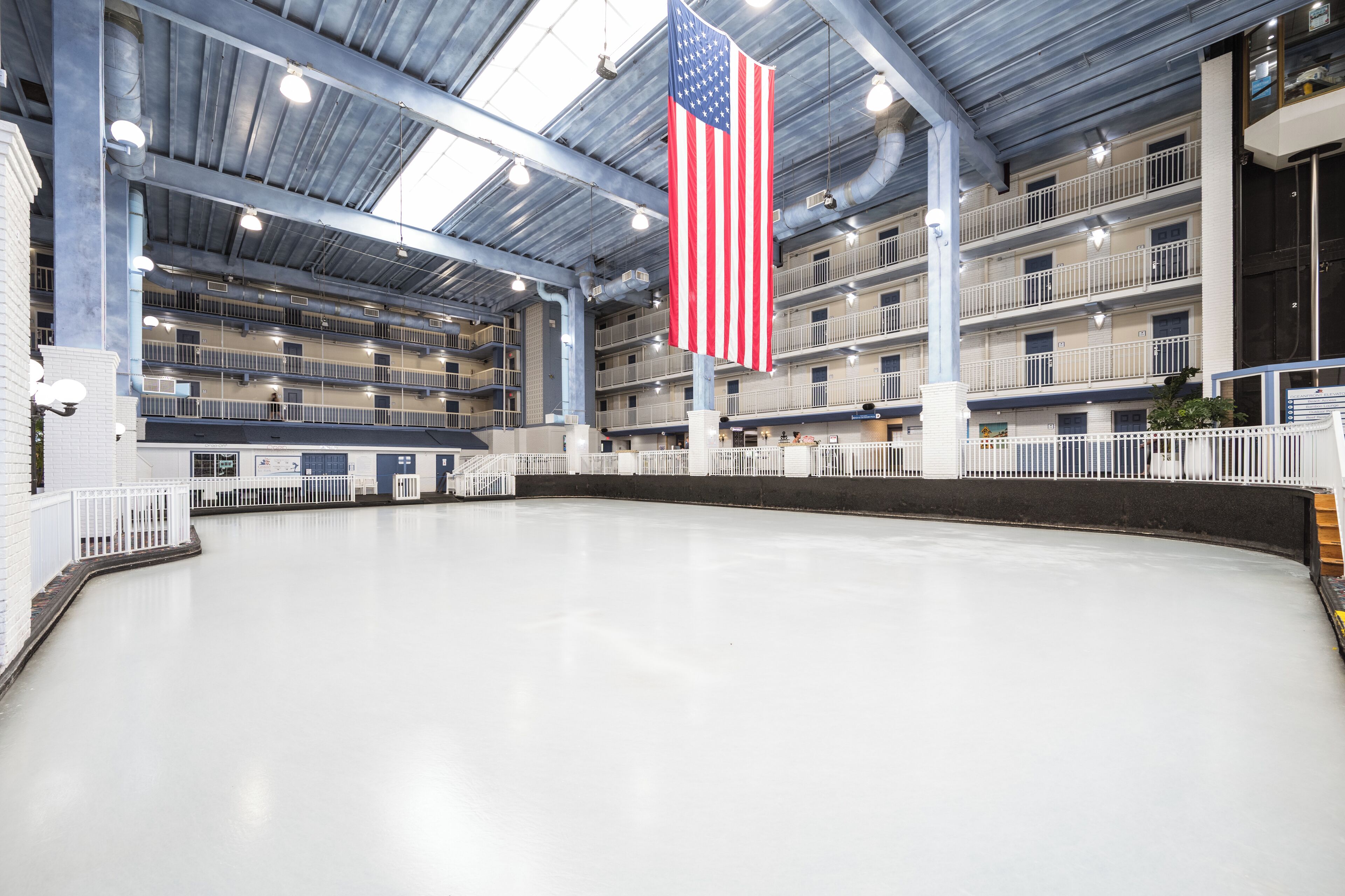 A multi-level indoor swimming pool with a large American flag, balconies, and a clean, modern design.