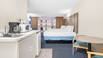 A hotel room with a bed, a small table, a kitchenette, and a view of the building's interior.