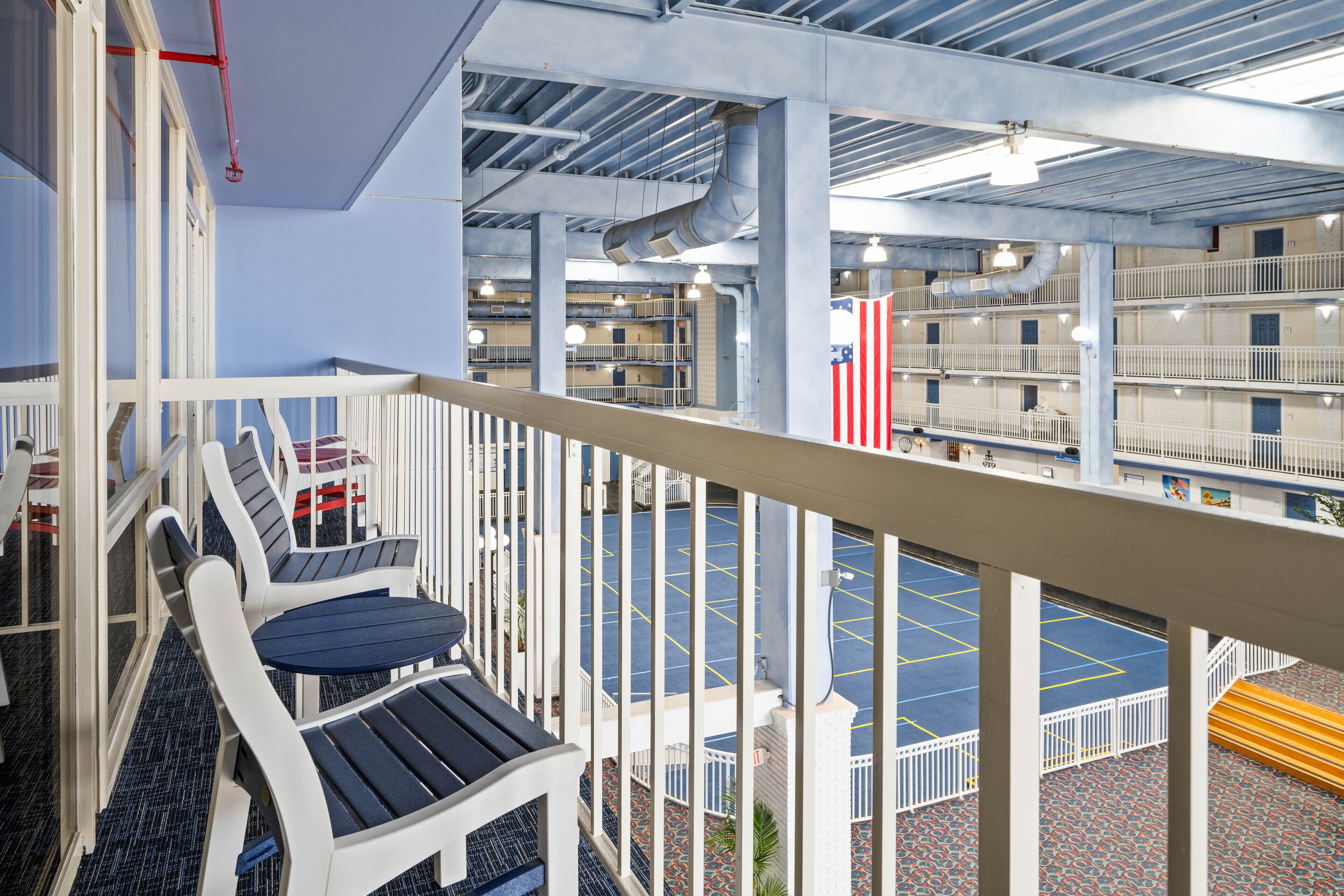 A balcony with white railings, a blue and white chair, and a view of a multi-level parking area with American flags.