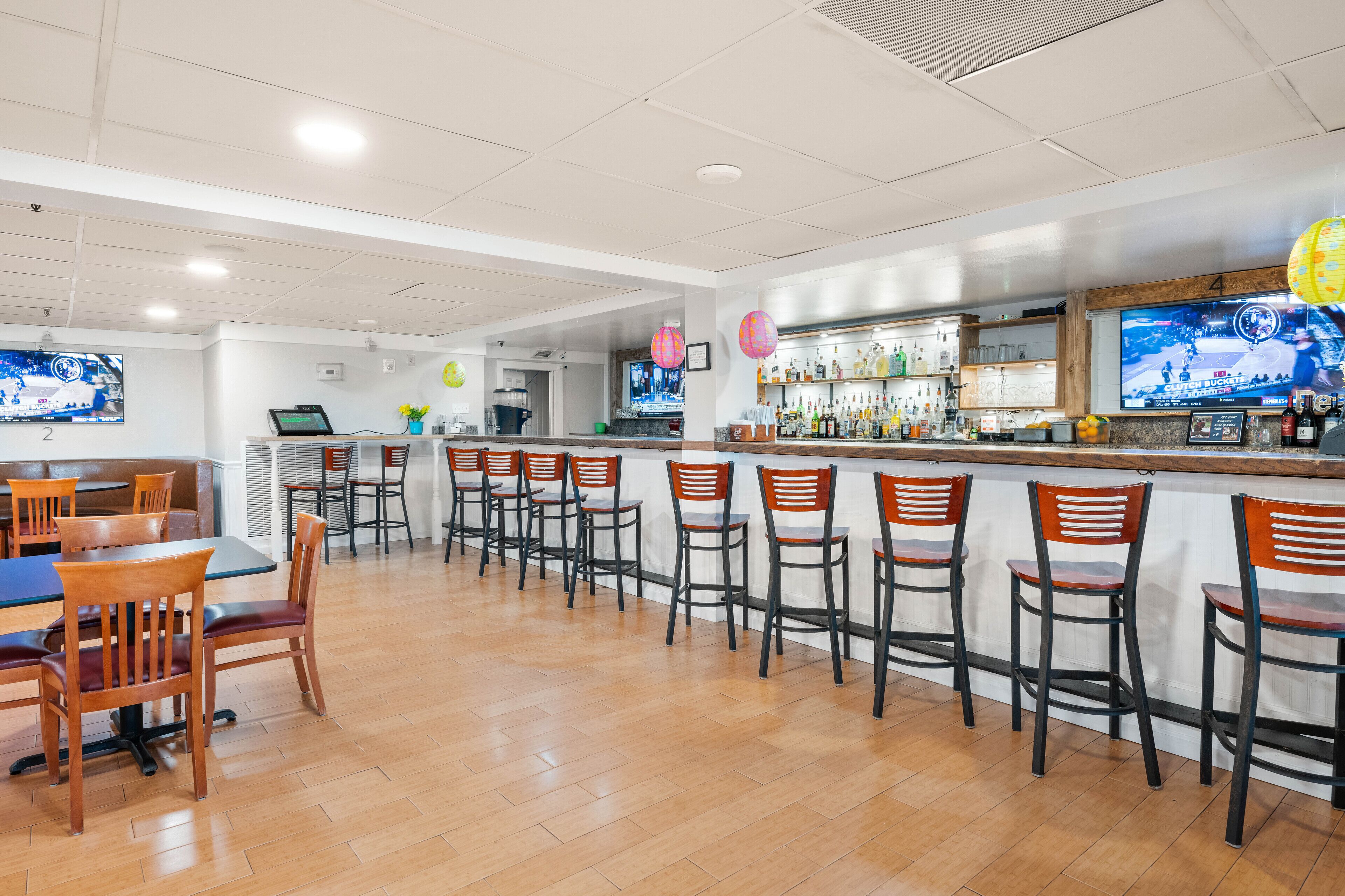 Un restaurante con zona de bar, varias opciones de asientos, incluyendo taburetes y mesas, y una pantalla de televisión que muestra un evento deportivo.