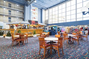 Relax in a spacious indoor area with high ceilings and large windows, featuring multiple seating areas and food and beverage kiosks.