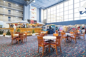 Relax in a spacious indoor area with high ceilings and large windows, featuring multiple seating areas and food and beverage kiosks.