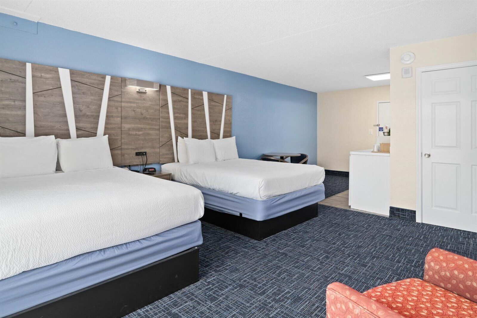 A hotel room with two beds, a desk, a chair, and a minibar.