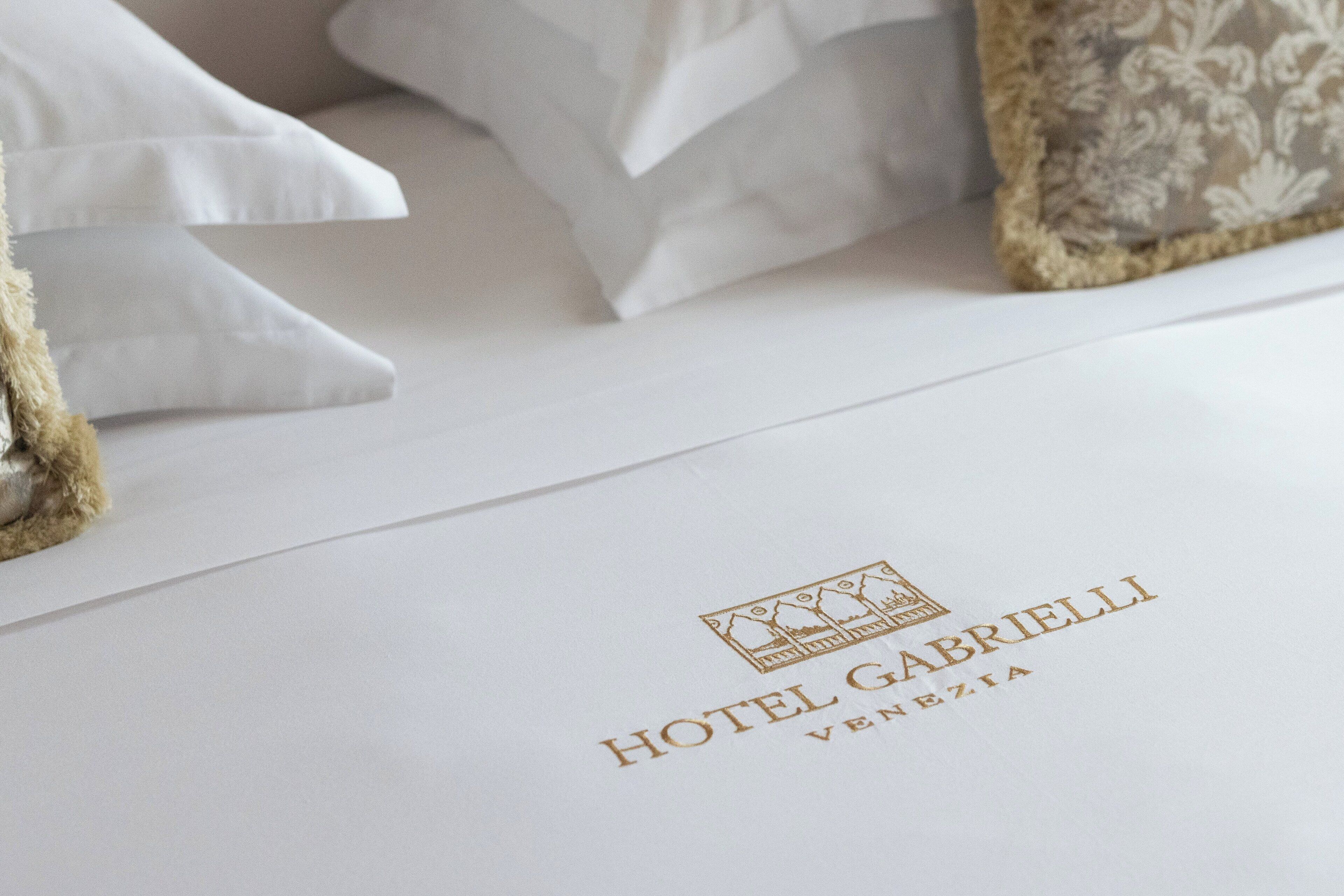 A hotel room with a neatly made bed, pillows, and a white envelope with the hotel name and location.