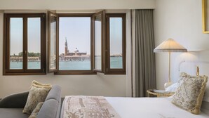 A hotel room with a bed, a sofa, a lamp, and a view of a historic building across the water. - Hotel Gabrielli - Starhotels Collezione  (Venice)