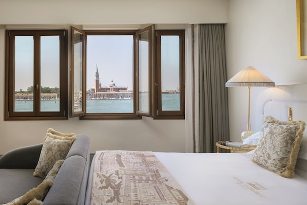 Ein Hotelzimmer mit Bett, Sofa, Lampe und Blick auf ein historisches Gebäude am Wasser.