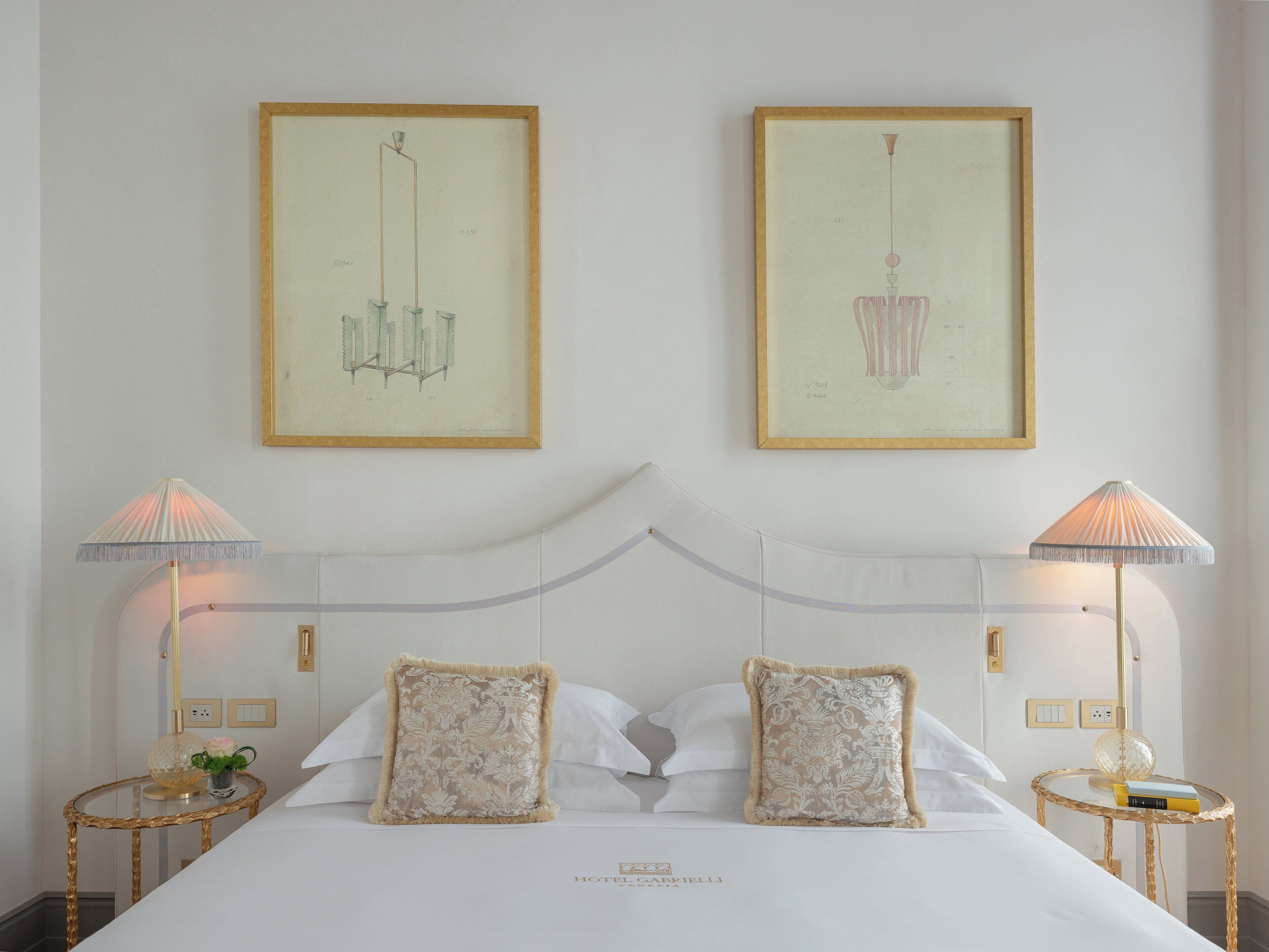 Ein Hotelzimmer mit einem Bett, zwei Nachttischlampen und zwei gerahmten Kunstwerken an der Wand.