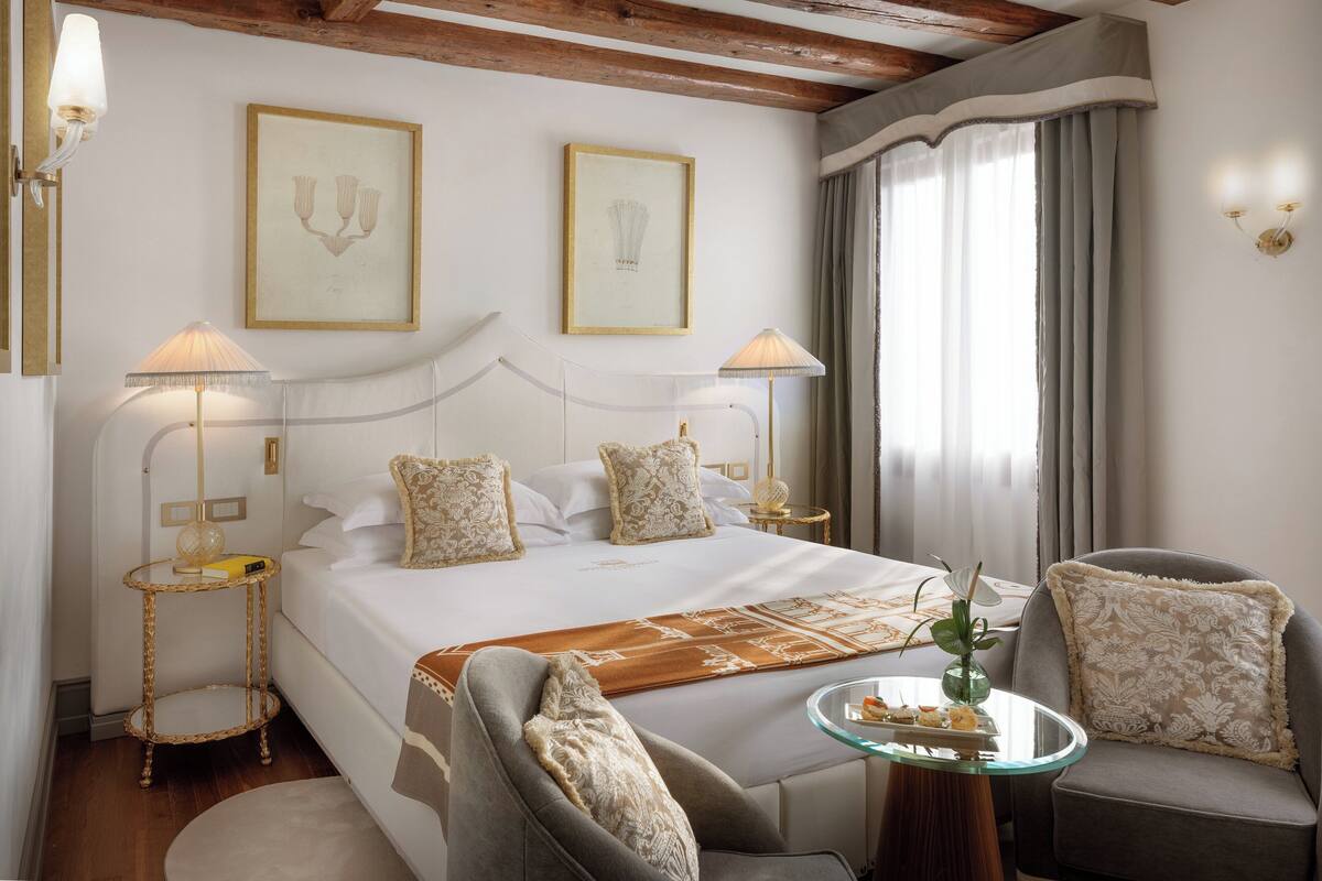 Une chambre d’hôtel avec un grand lit, deux lampes de chevet, une petite table avec un vase et une chaise.