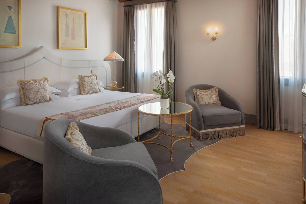 Une chambre d’hôtel avec un grand lit, un coin salon comprenant un fauteuil et une petite table, ainsi qu’un vase avec des fleurs.