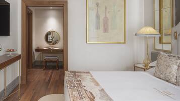 A hotel room with a bed, a desk, a chair, a mirror, and a wall-mounted lamp.