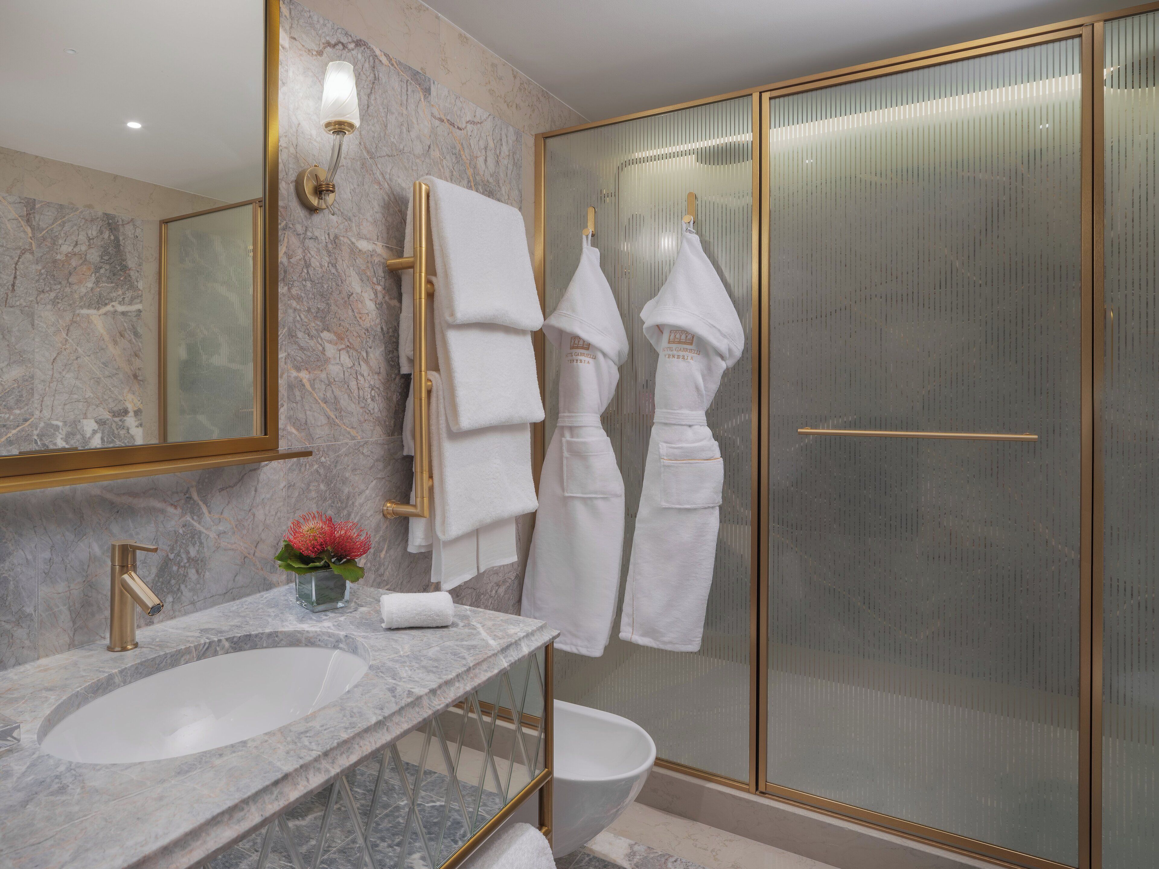 A modern bathroom with a marble vanity, a gold-framed mirror, and a glass-enclosed shower area.