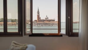 A room with a large window overlooking a historic building with a tower and dome, a body of water, and boats. - Hotel Gabrielli - Starhotels Collezione  (Venice)