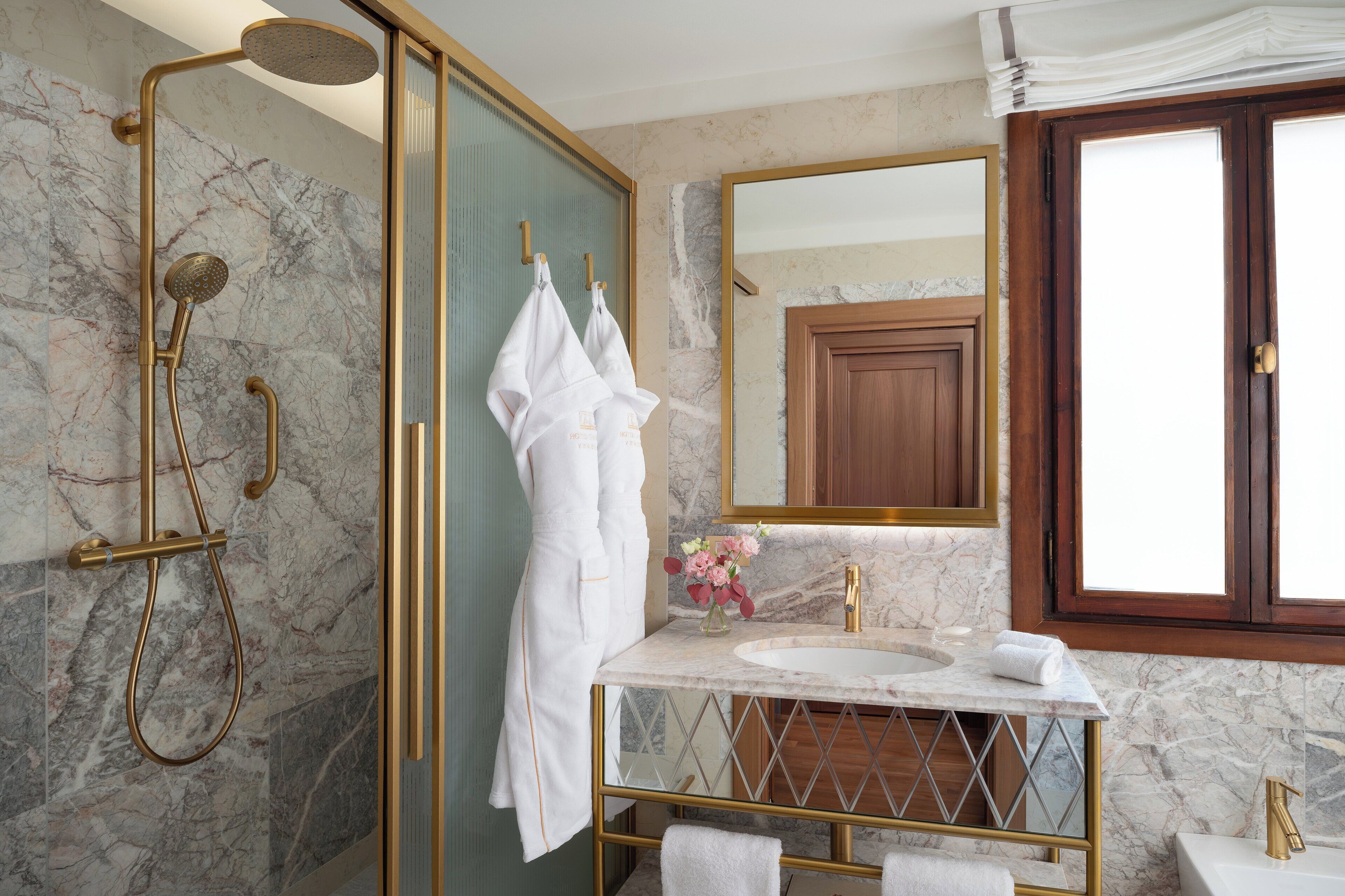 A bathroom with a marble shower, a large mirror, and a gold-framed vanity.