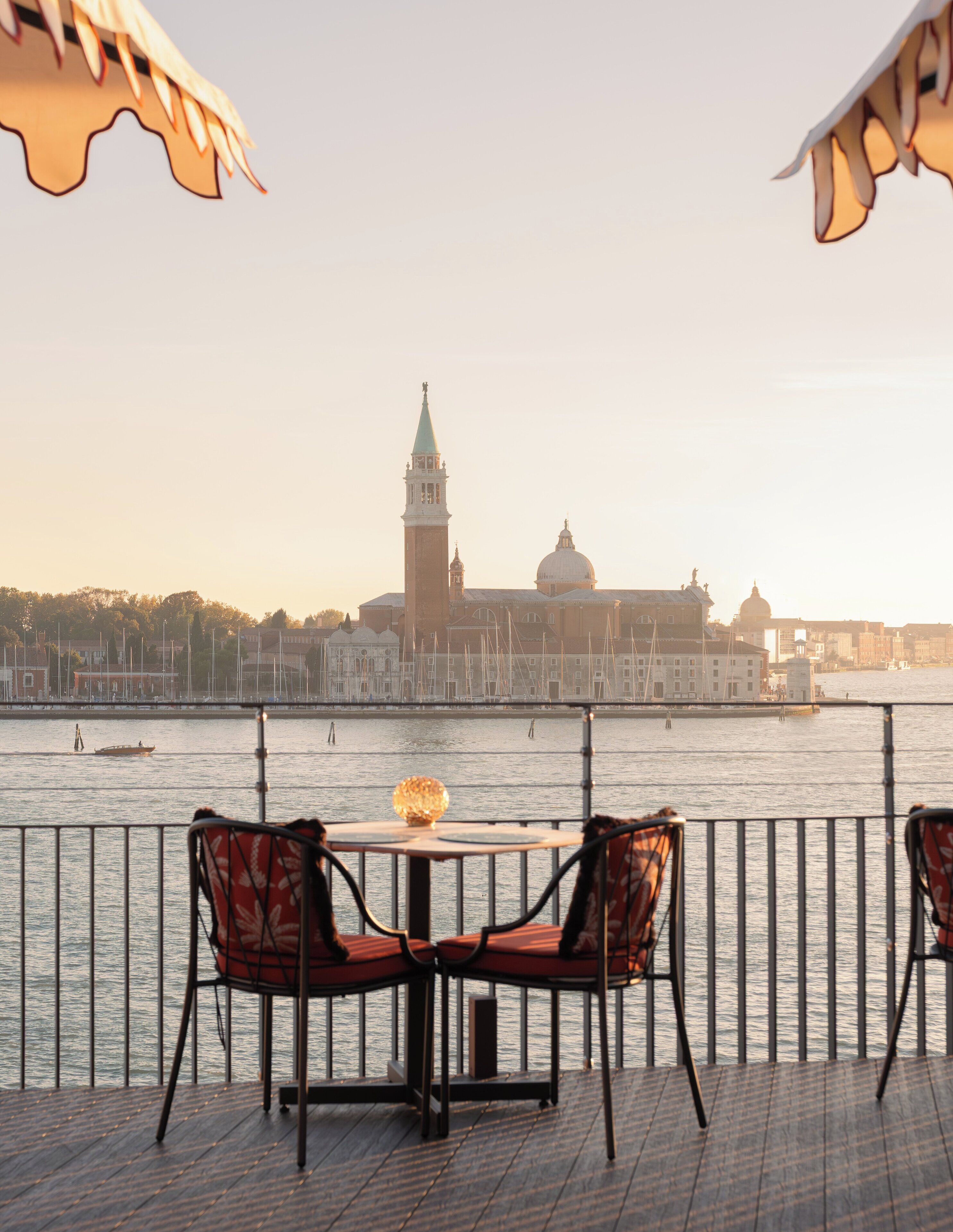 A table and chairs on a deck with a view of a historic building across the water.