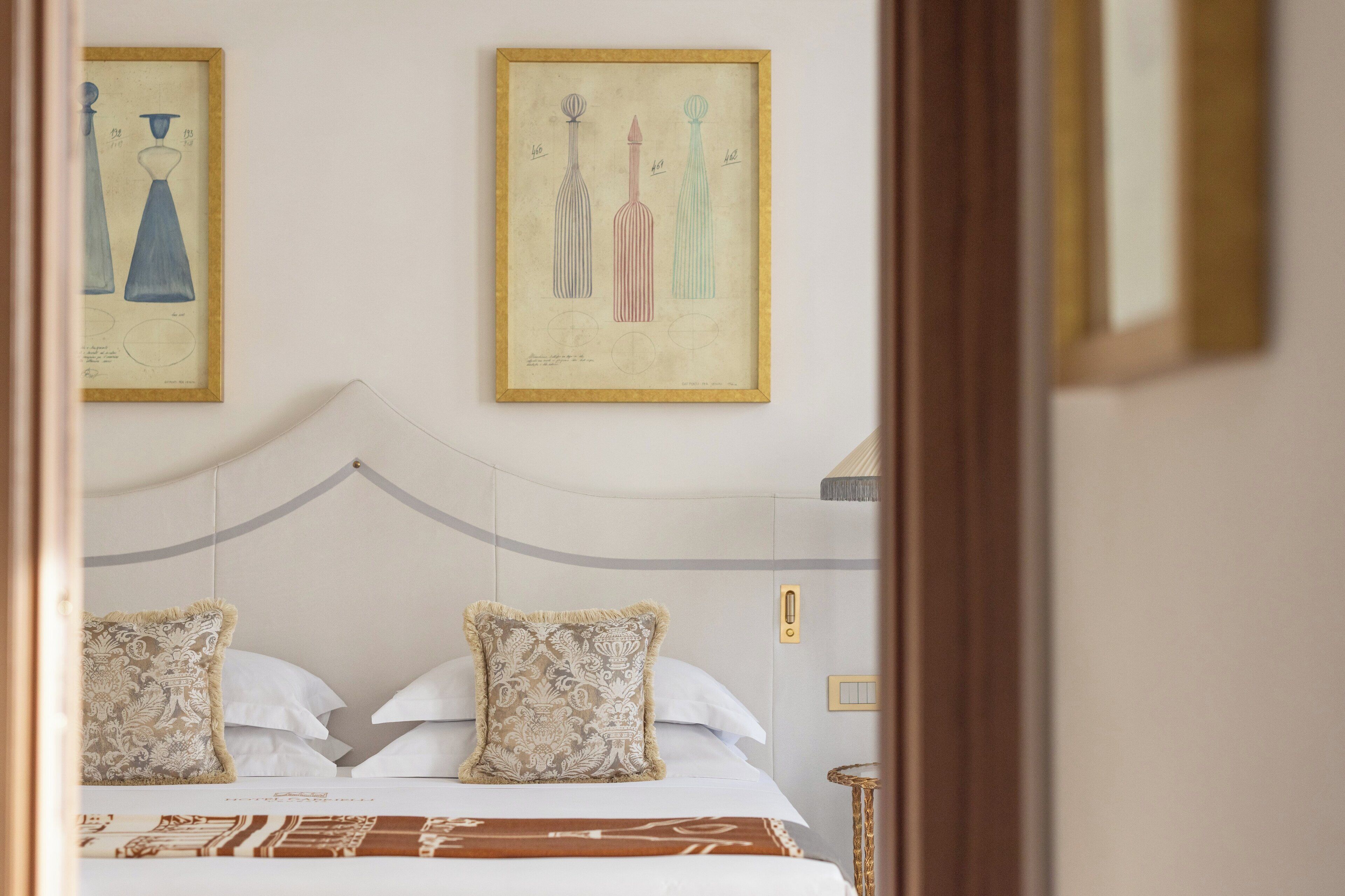 A hotel room with a bed, two pillows, a bedside table, and two framed artworks on the wall.