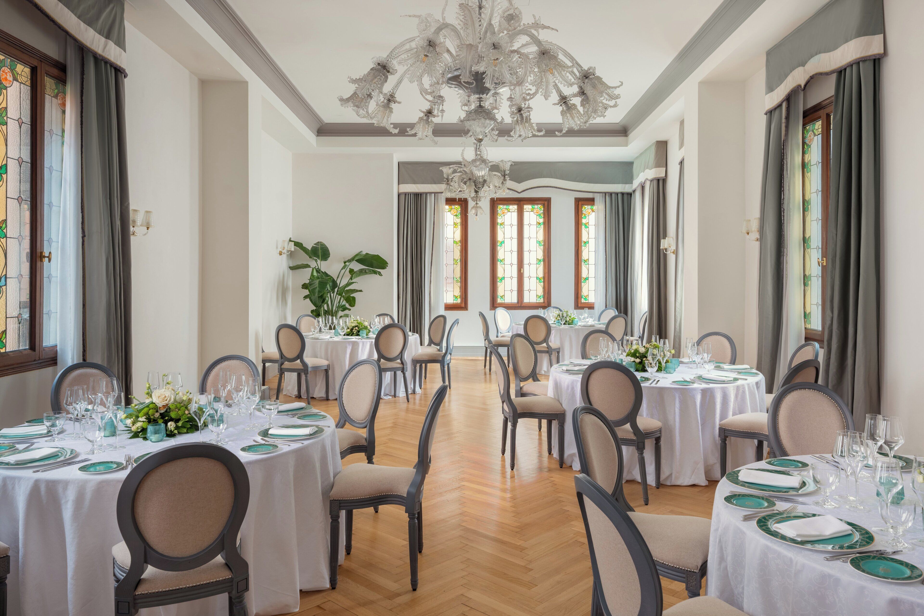 Un comedor con mesas redondas, sillas y una lámpara de araña.