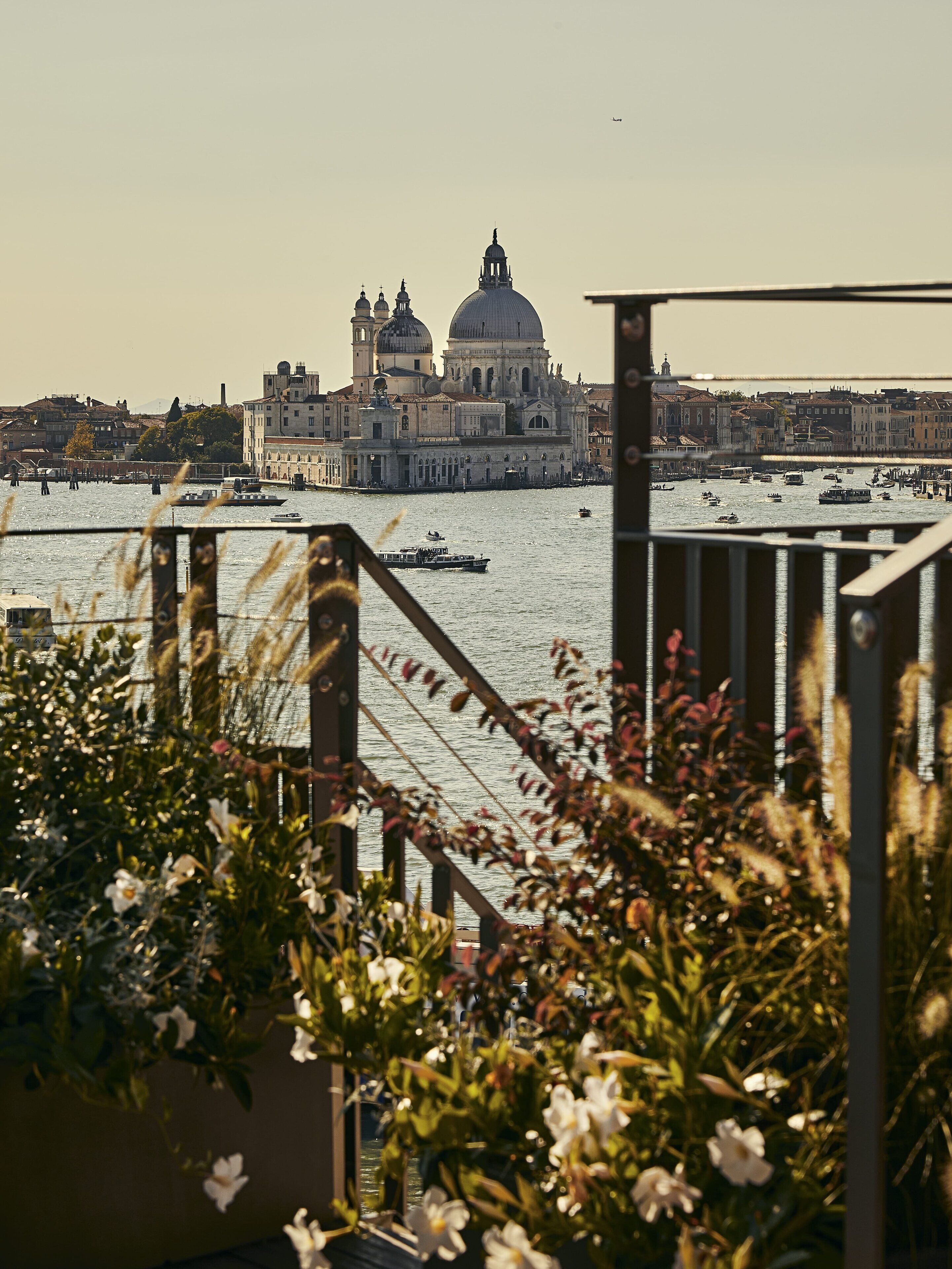 A view of a historic building with domes and a large bell tower across the water, with boats and a bridge in the foreground.