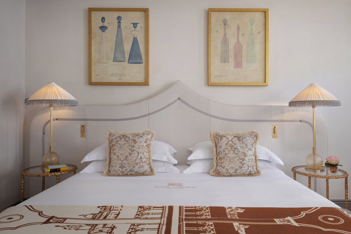 A hotel room with a large bed, two bedside tables, two lamps, and two framed botanical illustrations on the wall.