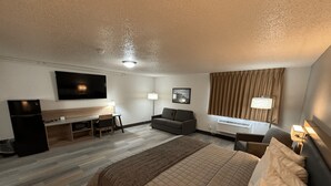 A hotel room with a bed, a desk, a television, a couch, and a window with curtains.