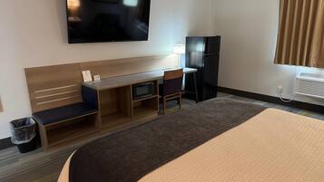 A hotel room with a bed, a desk, a television, a refrigerator, and a window with curtains.